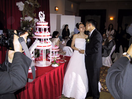 The groom pecks the bride next to the ginormous cake.